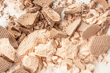 Eyeshadows of neutral beige and brown shades are scattered on a light surface. Detailed macro photo. The concept of decorative cosmetics.