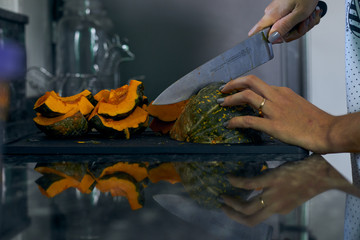 Obraz premium Calabaza siendo cortada por manos femeninas sobre tabla en concina oscura.
