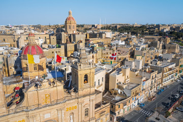 Aerial top view of Birgu city. Main catholic church, red dome and many flags on the roofs. Clear blue sky. Malta island