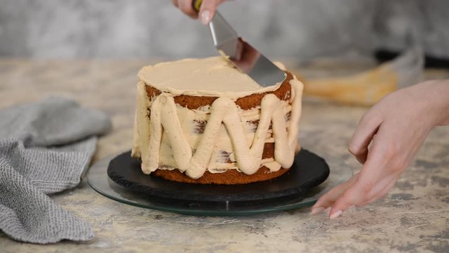 Girl making a cake in a bakery. Baker squeezes cream onto a cake layer.