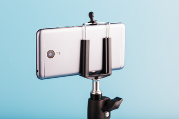 The smartphone is mounted on a tripod as a photo-video camera for a blog on a blue background. Record videos and photos.