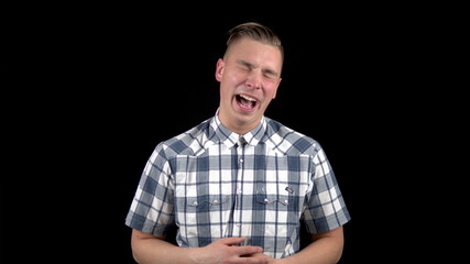 The young man shows the emotion of laughter. A man is laughing in a shirt on a black background