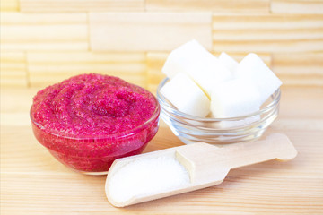 Natural pink body scrub made from sugar. Pink scrub in a glass cup on a background of candles and sugar.