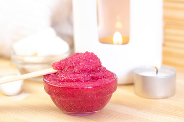 Fototapeta na wymiar Natural pink body scrub made from sugar. Pink scrub in a glass cup on a background of candles and sugar.