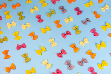 Italian pasta pattern on a blue background. Various colors of bow tie farfalle pasta viewed from above. Top view. Repetition.