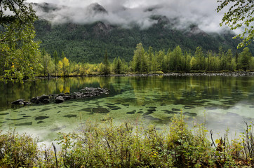On the shore of a mountain lake, stones and forest. cloudy day, natural light