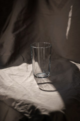 Composition glass cup half filled with water on a cloth background. Hard light. Trend color.