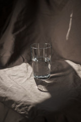 Composition glass cup half filled with water on a cloth background. Hard light. Trend color.