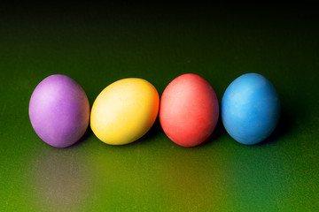 Colorful gypsum easter eggs on green background in a row with reflected color.
