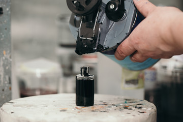 Naklejka premium The painter’s hands are holding a can of paint on which a mix cover for a mix installation is put on. Under the can is a full bottle of dark paint.