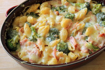Melted cheddar cheese over pasta shells with ham and broccoli bake in an oven dish.