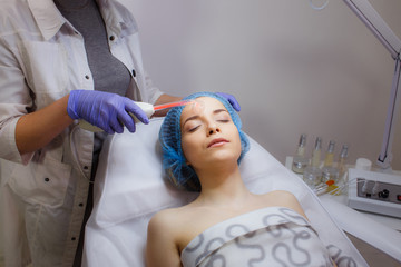 Obraz na płótnie Canvas A young woman visited a dermatologist. Receiving electric darsonval facial massage procedure at beauty salon.