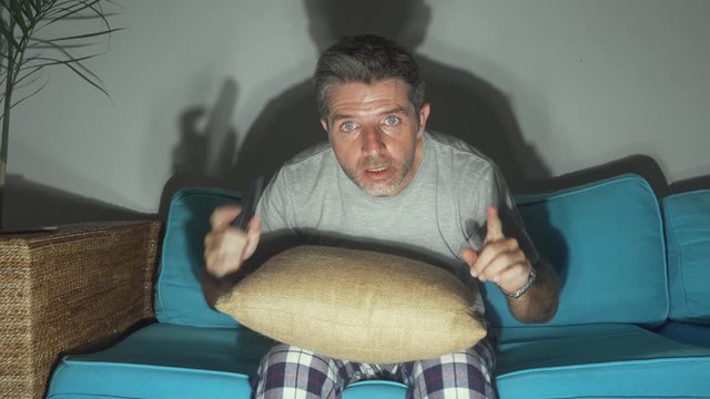 attractive and excited football fan man watching soccer game on TV celebrating scoring goal crazy happy screaming cheering his team at home living room couch gesturing in spastic celebration
