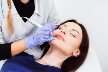 Fototapeta premium Young woman having permanent makeup on lips in beautician salon. Close up