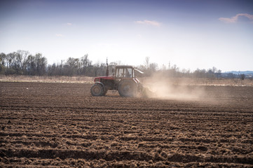 Naklejka premium Farmer in tractor preparing land with seedbed cultivator in early spring