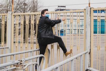 man in medical mask climb over the fence, refugee concept, coronavirus quarantine.