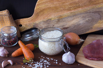 rice in a glass jar and ingredients for cooking pilaf on a wooden table
