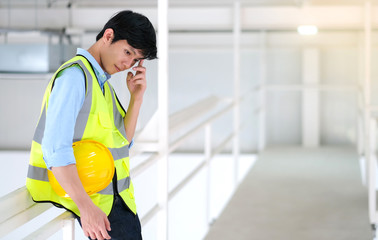 Junior engineer standing in the plant holding helmet with copy space. Wearing safety vest. Feeling happy and smile on work. Engineering and design concept.