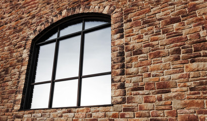large arch-shaped window with reflective glass and a binding on a stone wall. Copy space for...