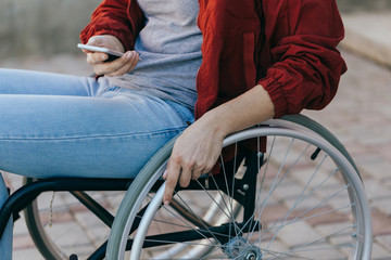 Obraz premium A woman in a wheelchair with a phone in her hand walks on the street, her hand is close up, an unrecognizable man.