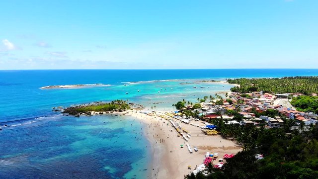 Majestic aerial shot of Morro de Sao Paulo blue turquoise beaches, tourists enjoying the beach and sun, and green nature. Bahia, Brazil. Drone slowly moving forward
