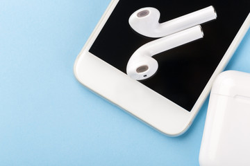 Wireless bluetooth headphones with a modern mobile phone on a blue background.