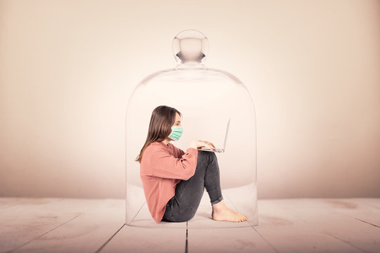 young girl with face mask using a laptop in a glass container. Coronavirus continuation concept.