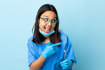 Young brunette mixed race dentist woman holding tools over isolated background pointing to the side to present a product and whispering something