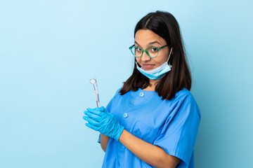 Young brunette mixed race dentist woman holding tools over isolated background scheming something