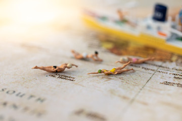 Miniature people : Young in swimsuit and friends swiming on world map. Image use for holiday, vacation concept.