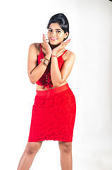Young woman in a bright red dress leaning and looking ahead and cupping her face with both hands with a bright smile