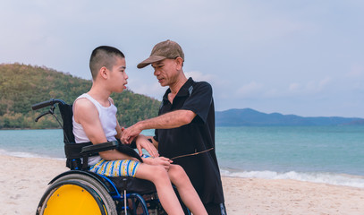 Obraz na płótnie Canvas Asian special child and Father in wheelchair on the beach with daylight, They are happiness in holidays with the travel, Life in the education age of disabled children, Happy disability kid concept.