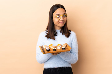 Young brunette mixed race woman holding sushi over isolated background scheming something