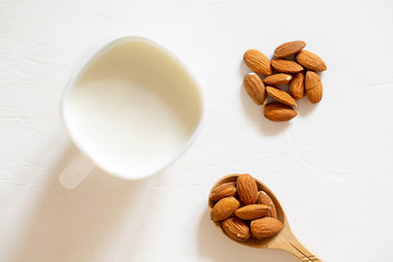 Nut almonds in a wooden spoon on a white background. Almond seed milk in a glass bowl.