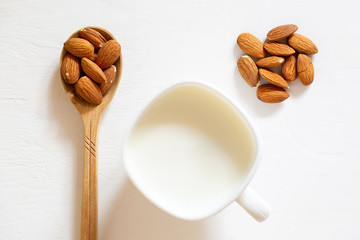 Nut almonds in a wooden spoon on a white background. Almond seed milk in a glass bowl.