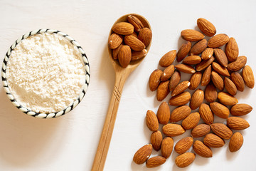 Nut almonds in a wooden spoon on a white background. Natural almond seed flour in a glass bowl.