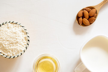 Natural flour, oil and almond seed milk in a glass bowl. Nut almonds in a wooden spoon on a white background.