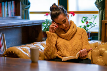 On the couch in front of the window, a woman caught up in reading.