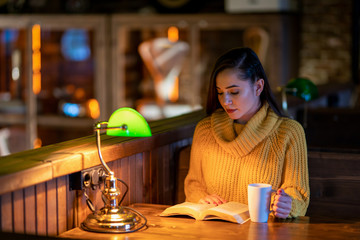 The woman at the table drinking coffee and reading a book