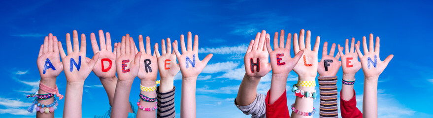Kids Hands Holding Colorful German Word Anderen Helfen Means Help Others. Blue Sky As Background