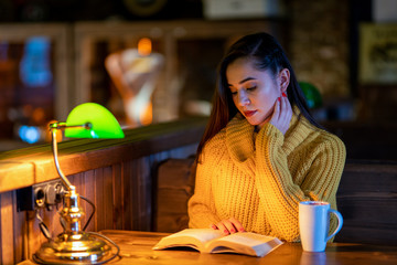 The woman at the table drinking coffee and reading a book