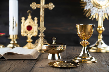 Fototapeta na wymiar Catholic religion concept. Catholic symbols composition. The Cross, monstrance, Holy Bible and golden chalice on wooden altar and gray background. 