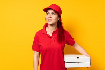 Pizza delivery girl holding a pizza over isolated background thinking an idea while looking up