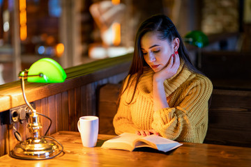 The woman at the table drinking coffee and reading a book