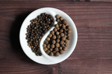 Black pepper corns and allspice  in Yin Yang shaped bowl on wooden background