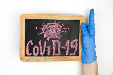 Covid-19 word written on a small blackboard hold woman hands in blue medical glove. Protection concept