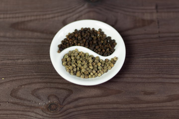 Black and green pepper corns in Yin Yang shaped bowl on brown wooden background