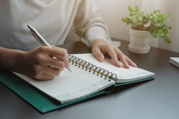 The hand of a young woman writing note of the warning message, details, things to do or preparation information of report with a bronze pen onto the book used eye preservation paper, green cover page