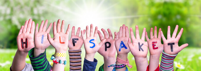 Children Hands Building Colorful German Word Hilfspaket Means Aid Package. Sunny Green Grass Meadow As Background