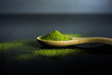 Matcha green tea powder on wooden spoon on black background.